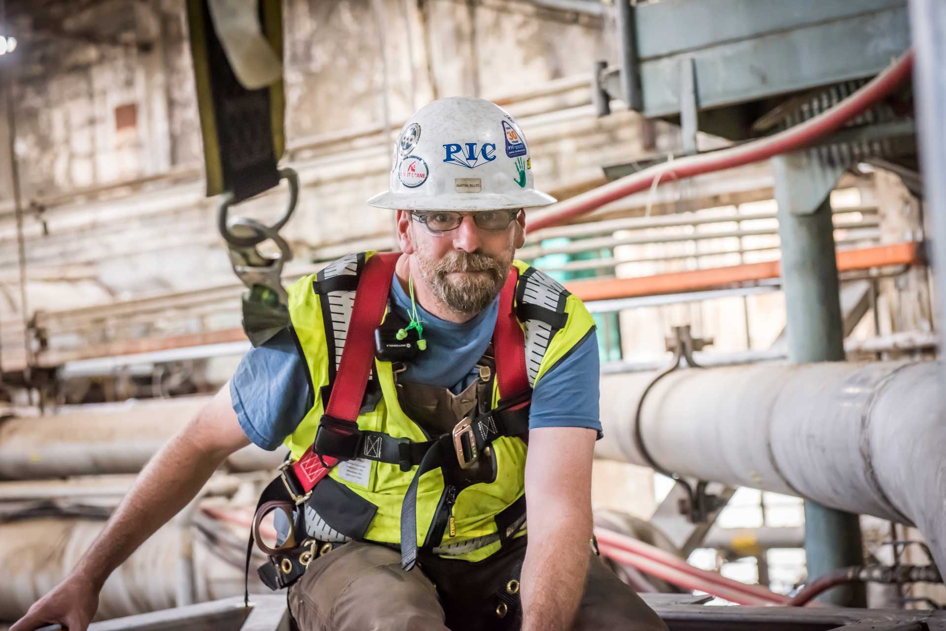 Picture of an industrial worker sitting among industrial piping, looking at the camera